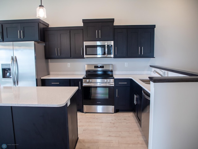 kitchen featuring appliances with stainless steel finishes, light hardwood / wood-style flooring, hanging light fixtures, and sink