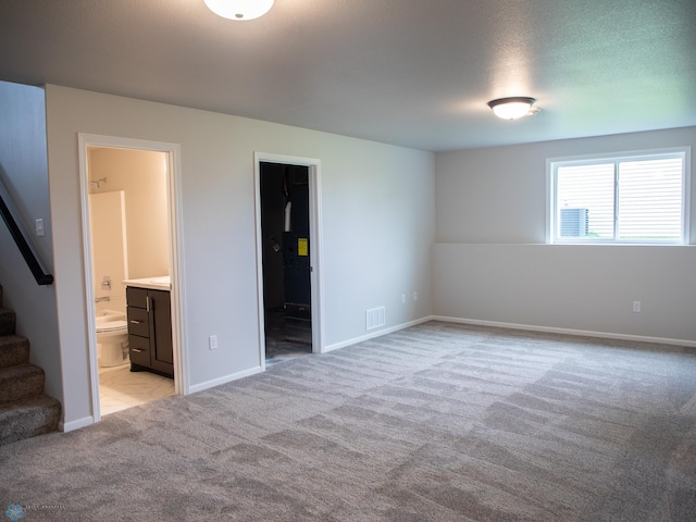 unfurnished bedroom featuring ensuite bathroom, a walk in closet, a textured ceiling, light colored carpet, and a closet