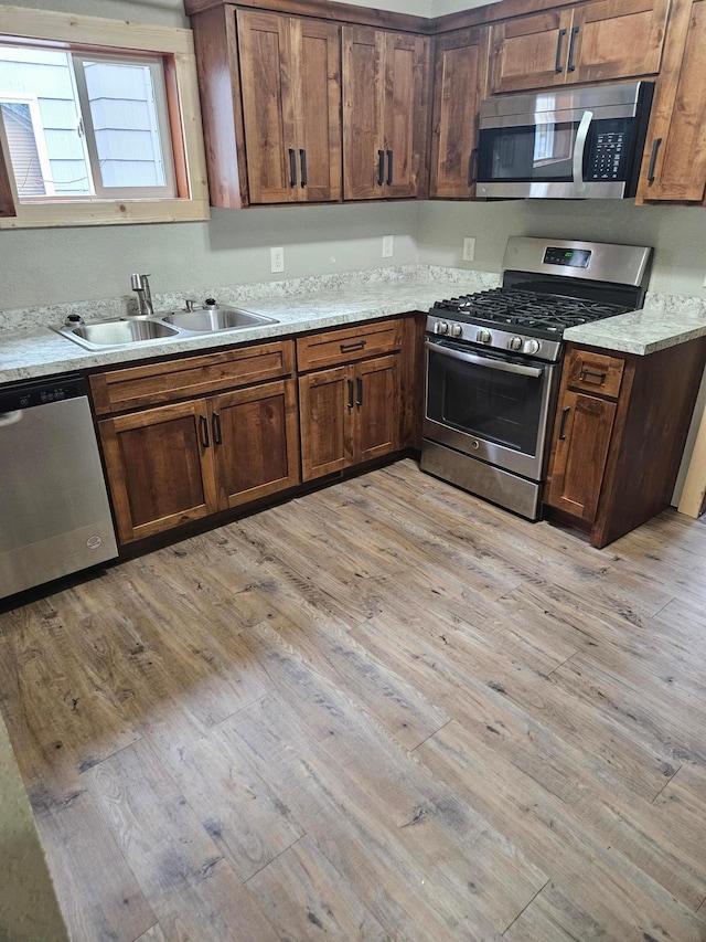 kitchen featuring sink, light stone countertops, stainless steel appliances, and light hardwood / wood-style flooring