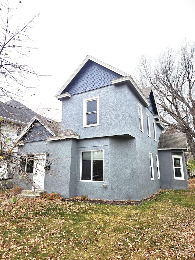 rear view of house with a lawn and stucco siding