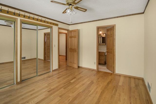 unfurnished bedroom with crown molding, two closets, a textured ceiling, and light hardwood / wood-style flooring