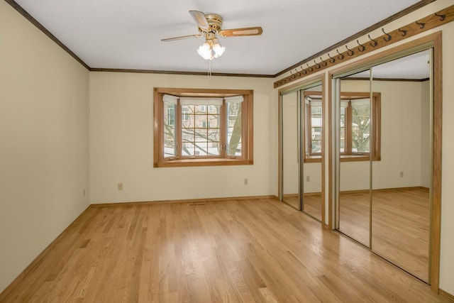 unfurnished bedroom featuring two closets, ornamental molding, ceiling fan, and light wood-type flooring