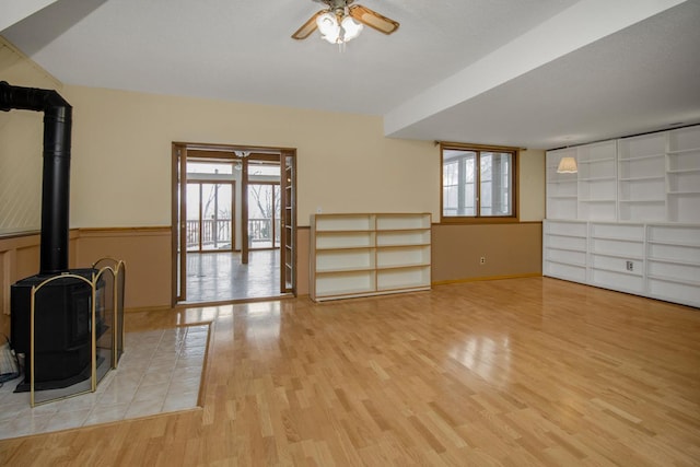 unfurnished living room featuring ceiling fan, a wood stove, a wealth of natural light, and light hardwood / wood-style floors