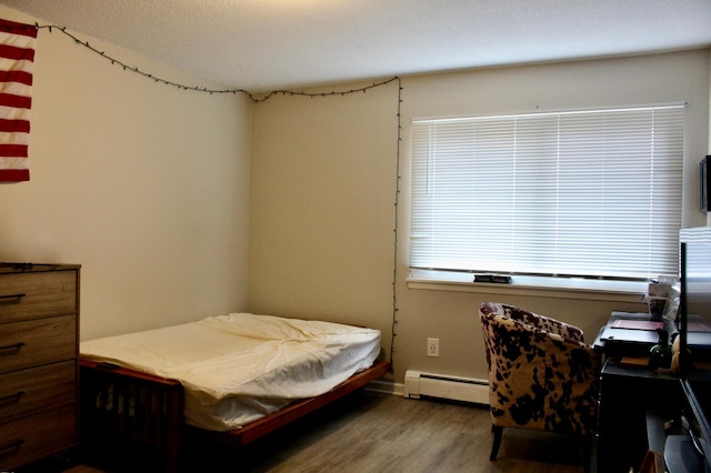 bedroom featuring hardwood / wood-style flooring and a baseboard heating unit