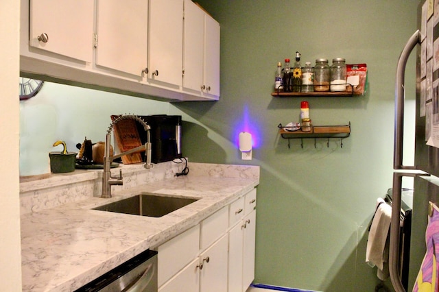 kitchen featuring white cabinets, stainless steel dishwasher, light stone countertops, and sink