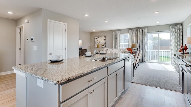 kitchen featuring light hardwood / wood-style floors, light stone countertops, sink, and an island with sink