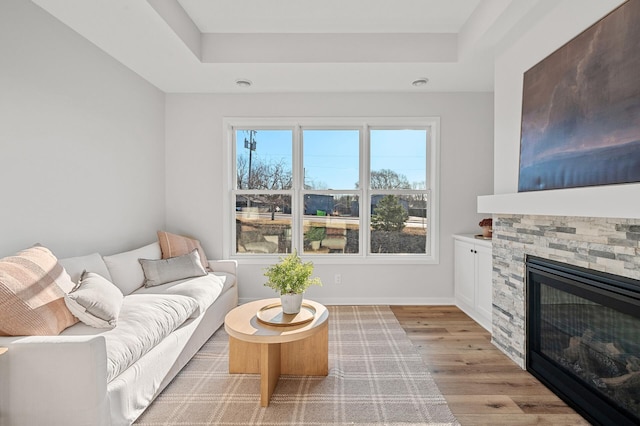 living room with a stone fireplace, a tray ceiling, and light hardwood / wood-style floors