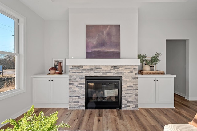 unfurnished living room with light hardwood / wood-style floors, a stone fireplace, and plenty of natural light