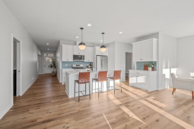 kitchen with appliances with stainless steel finishes, a center island, white cabinetry, pendant lighting, and light hardwood / wood-style flooring