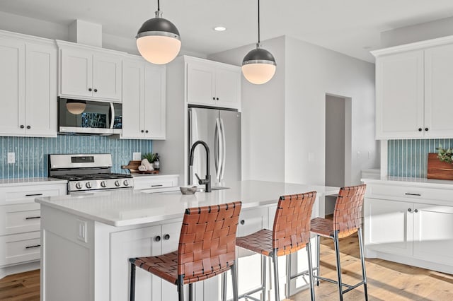 kitchen with a kitchen bar, white cabinets, decorative light fixtures, and stainless steel appliances