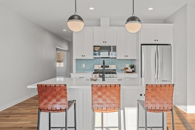 kitchen featuring stainless steel appliances, light hardwood / wood-style flooring, a kitchen bar, and white cabinets