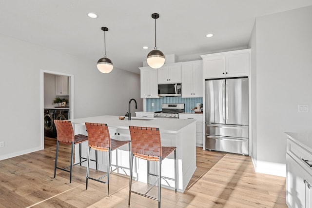 kitchen featuring a center island with sink, appliances with stainless steel finishes, a kitchen breakfast bar, white cabinetry, and light hardwood / wood-style flooring