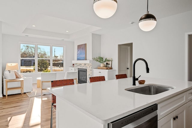 371 Liberty Dr, Hanover, MN 55341 - kitchen with light wood-style flooring, stainless steel dishwasher, a tiled fireplace, a sink, and white cabinetry