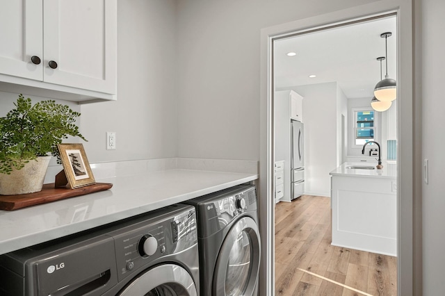 clothes washing area featuring cabinets, light hardwood / wood-style flooring, sink, and washer and clothes dryer