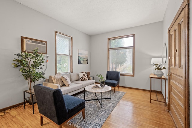 living room with a textured ceiling, a wall mounted air conditioner, and light wood-type flooring