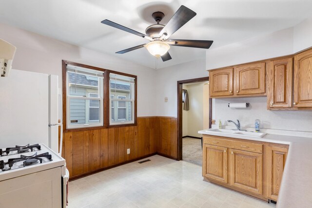 kitchen featuring wooden walls, sink, ceiling fan, and white appliances