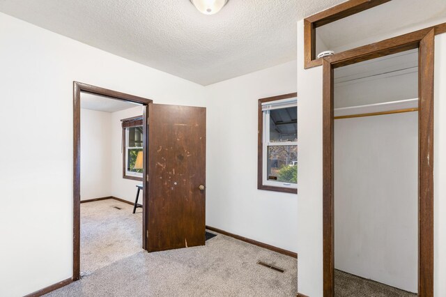 unfurnished bedroom with a closet, light colored carpet, a textured ceiling, and multiple windows