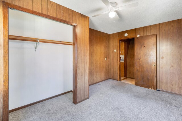 unfurnished bedroom featuring ceiling fan, wood walls, light colored carpet, a textured ceiling, and a closet