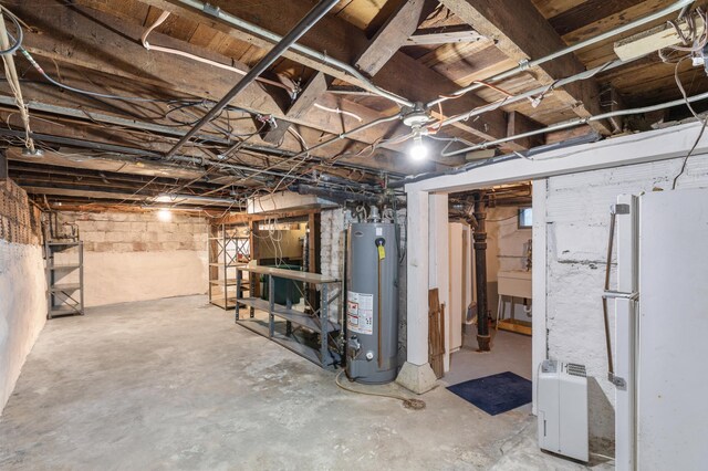 basement featuring sink, gas water heater, and white refrigerator