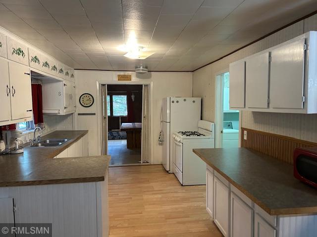 kitchen with washer / clothes dryer, light hardwood / wood-style flooring, white gas range oven, sink, and white cabinetry