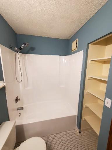 bathroom with  shower combination, a textured ceiling, and toilet