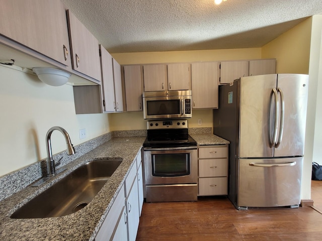 kitchen with dark stone counters, sink, dark hardwood / wood-style floors, a textured ceiling, and appliances with stainless steel finishes