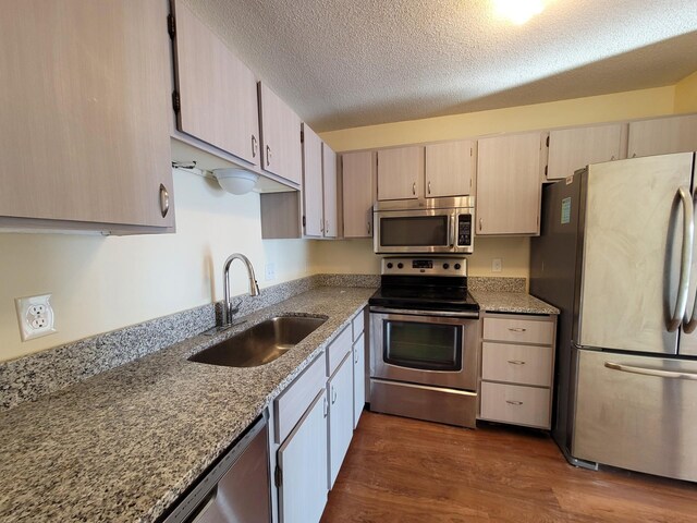 kitchen featuring light stone countertops, a textured ceiling, stainless steel appliances, sink, and dark hardwood / wood-style floors