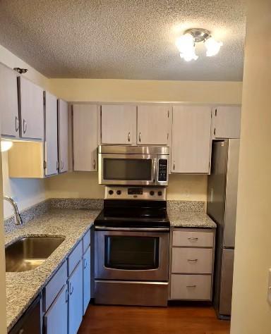 kitchen with sink, light stone counters, dark hardwood / wood-style floors, a textured ceiling, and appliances with stainless steel finishes