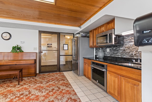 kitchen featuring tasteful backsplash, stainless steel appliances, sink, light tile patterned floors, and dark stone countertops