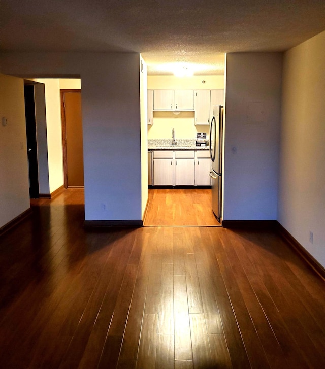 kitchen featuring dark wood-type flooring, sink, stainless steel fridge, light stone countertops, and a textured ceiling