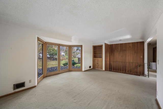 carpeted spare room with wood walls and a textured ceiling