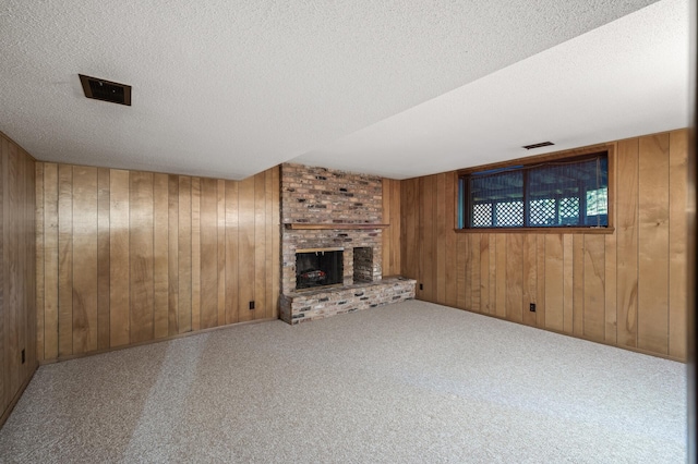 unfurnished living room featuring a brick fireplace, a textured ceiling, carpet floors, and wooden walls