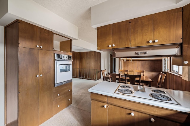 kitchen featuring wood walls, a textured ceiling, white appliances, and light carpet