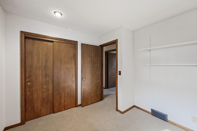 unfurnished bedroom featuring light colored carpet, a textured ceiling, and a closet