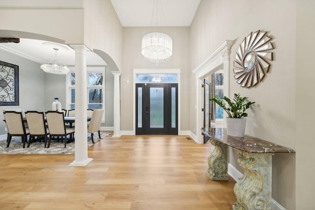 foyer featuring a towering ceiling, wood-type flooring, a chandelier, and decorative columns