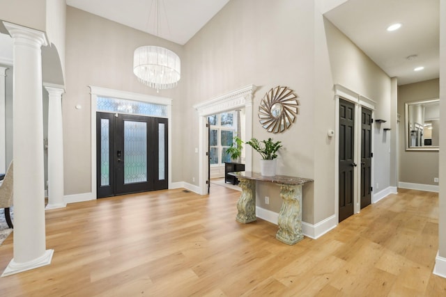 entrance foyer with a towering ceiling, ornate columns, light wood-type flooring, and a notable chandelier