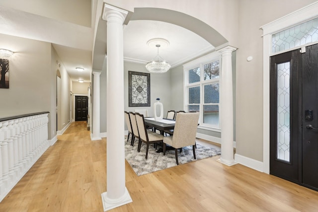 dining space featuring decorative columns, a chandelier, ornamental molding, and light hardwood / wood-style flooring