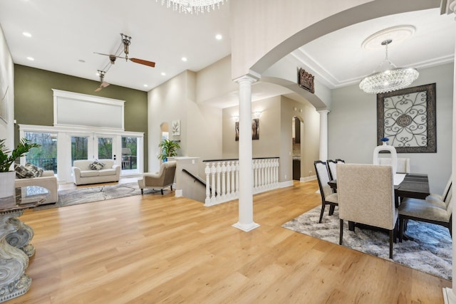 dining space with light wood-type flooring, ceiling fan with notable chandelier, a high ceiling, and decorative columns