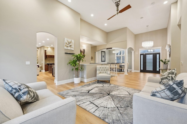 living room featuring a fireplace, a high ceiling, ceiling fan with notable chandelier, and light hardwood / wood-style floors