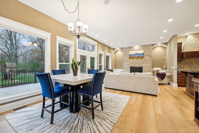 dining area with a fireplace, a wealth of natural light, light hardwood / wood-style floors, and an inviting chandelier