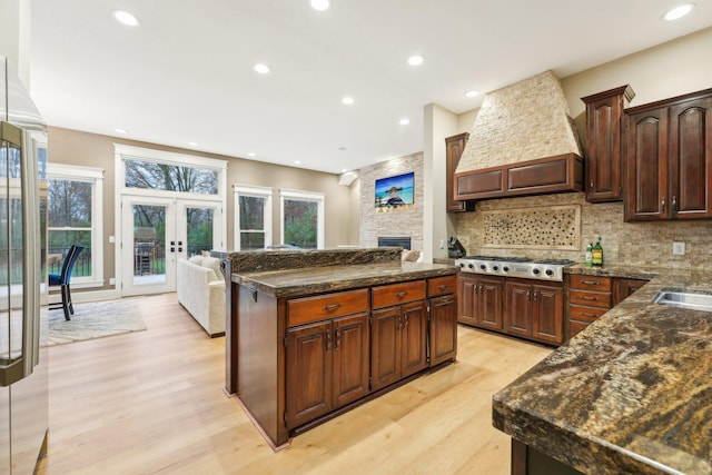 kitchen featuring stainless steel gas cooktop, backsplash, light hardwood / wood-style flooring, a kitchen island, and premium range hood