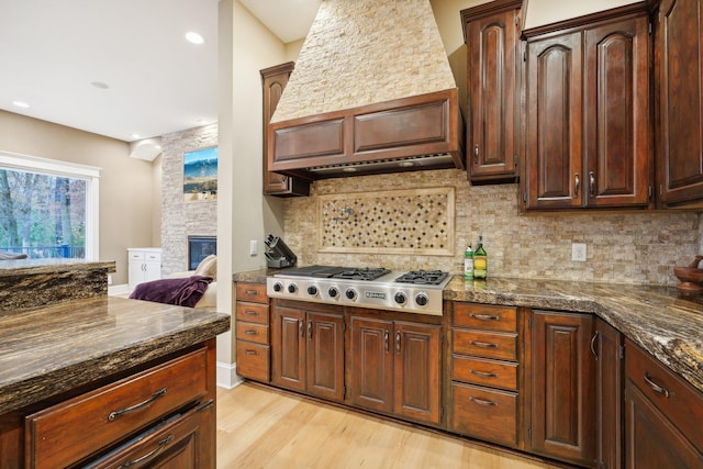 kitchen with stainless steel gas cooktop, backsplash, a fireplace, light hardwood / wood-style flooring, and premium range hood