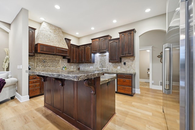 kitchen with stainless steel fridge, a kitchen island, dark brown cabinets, a kitchen breakfast bar, and light hardwood / wood-style flooring