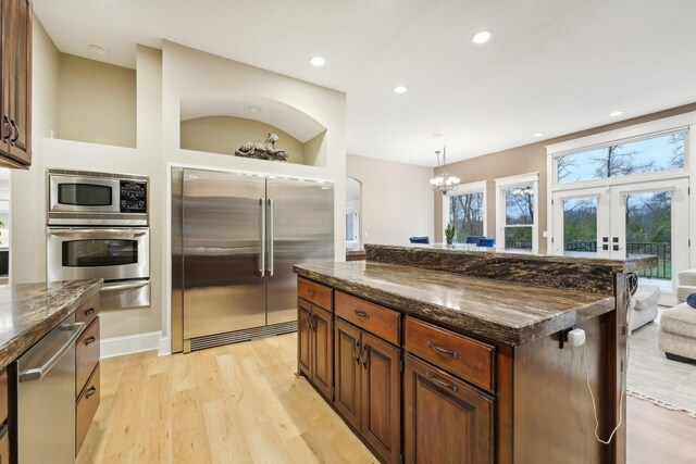 kitchen featuring a kitchen island, light wood-type flooring, appliances with stainless steel finishes, pendant lighting, and dark stone countertops