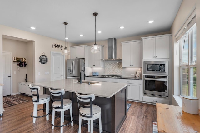 kitchen featuring decorative backsplash, appliances with stainless steel finishes, a sink, dark wood-style floors, and wall chimney exhaust hood