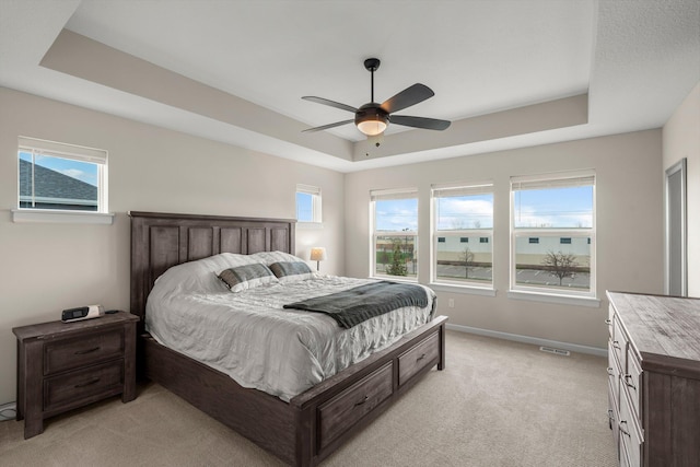 bedroom with visible vents, light carpet, baseboards, a tray ceiling, and a ceiling fan