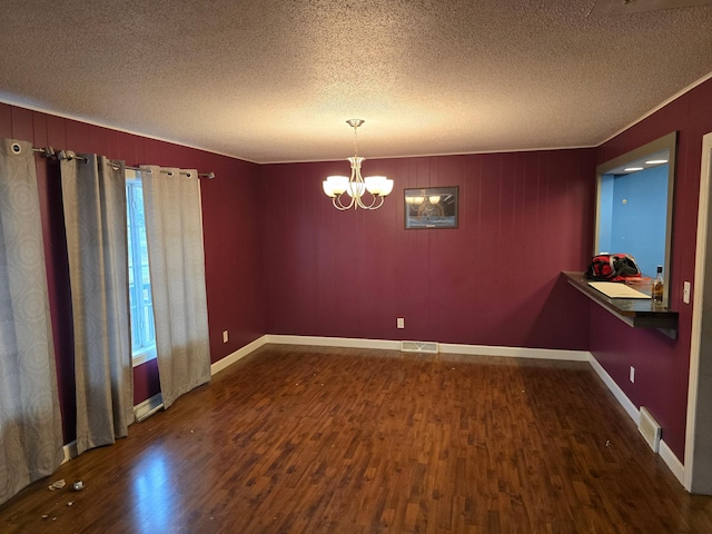 spare room with dark wood-type flooring, a chandelier, a textured ceiling, and ornamental molding