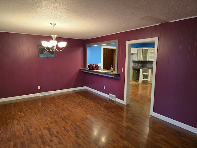 unfurnished room featuring wood walls, a textured ceiling, a notable chandelier, and dark hardwood / wood-style floors