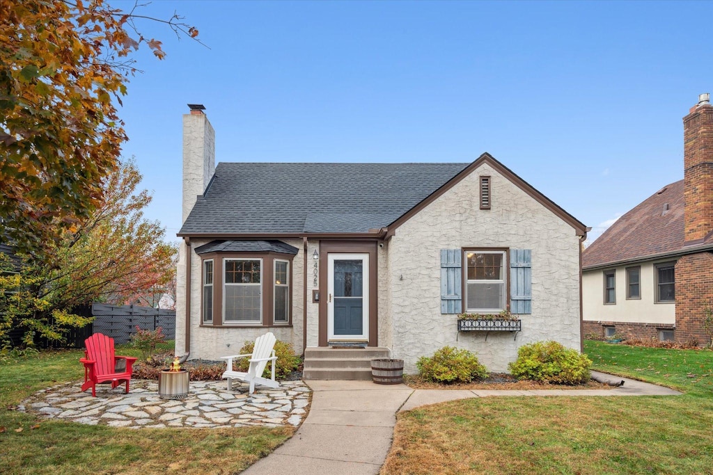 bungalow-style home with a fire pit, a front lawn, and a patio