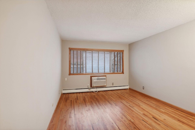 empty room featuring light hardwood / wood-style flooring, a baseboard heating unit, a wall mounted AC, and a textured ceiling